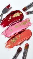 Colorful lipstick smears with gold leaf accents and makeup brushes on white background for beauty and cosmetics advertising campaigns.