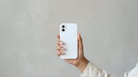 Hand holding white smartphone with dual camera setup against neutral background for mobile technology and communication concepts.