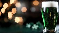 Green beer with foam head and shamrock decorations against dark background with festive bokeh lights. St Patrick's Day celebration concept.
