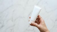 Close-up of hand holding blank white cosmetic tube against marble background for skincare, beauty product packaging mockup, and branding purposes.