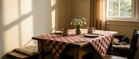 Rustic wooden dining table with red checkered tablecloth and fresh flowers in sunlit room, perfect for home decor and interior design projects.