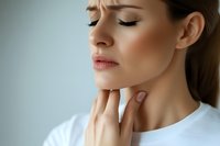 Young woman in white t-shirt touching her throat with painful expression, possibly experiencing sore throat or thyroid discomfort against light blue background.