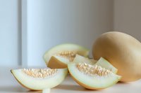 Sliced cantaloupe melon with seeds visible on white surface near whole fruit, suitable for food and nutrition content.