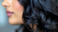 Young Asian woman with glossy black wavy hair and pink lips in profile view against blurred background, showcasing healthy, shiny hairstyle and natural makeup look.