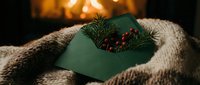Green gift box with pine branch and cone on cozy knit blanket by warm fireplace. Holiday present wrapping for Christmas celebration and winter festivities.