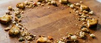 Wooden cutting board with scattered crushed nuts and crumbs forming circular border, overhead view with copy space for food preparation, cooking, or recipe content.