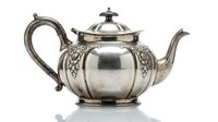 Antique silver teapot with ornate floral engravings and curved handle isolated on white background for vintage kitchen decor and elegant dining concepts.