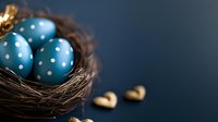 Blue polka dot Easter eggs in natural twig nest with decorative golden hearts against dark background, festive spring holiday composition.