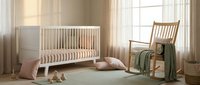 Serene nursery room with wooden crib, rocking chair, soft textiles, and natural light from windows, suitable for baby care and interior design projects.
