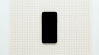Blank black smartphone with rounded corners isolated on grid paper background, ready for app design mockups and digital interface presentations.