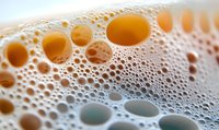 Macro shot of golden beer foam bubbles creating abstract pattern with light and shadow play. Fresh draught beer surface with varying bubble sizes.
