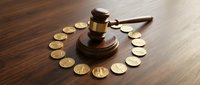 Wooden judge gavel surrounded by golden coins in circle on dark wood table representing legal fees, financial litigation, court costs and justice system.