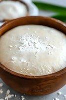 Fresh sourdough starter in wooden bowl showing active fermentation with bubbles and flour dusting on surface, macro food photography for baking and recipes.