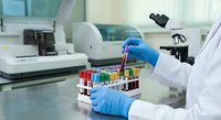 Laboratory technician in blue gloves handling test tubes with colorful samples in modern medical research facility with microscope and equipment.