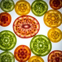 Colorful tomato slices in red, yellow and green varieties arranged on white background showing detailed seed patterns and translucent flesh for culinary designs.