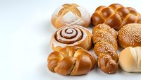Fresh baked bread assortment with croissants, braided challah, sesame rolls and cinnamon swirl pastries on white background for bakery menu design.