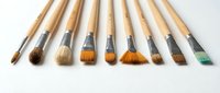 Professional artist paintbrushes with natural wooden handles arranged in row on white background for creative projects and artistic work.