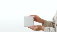 Close-up of hands holding blank white box against neutral background, suitable for product packaging mockups, branding presentations, and commercial advertising campaigns.
