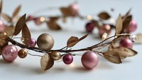 Festive garland with pink and gold glitter baubles, metallic leaves, and twinkling lights on delicate branches for holiday home decoration.
