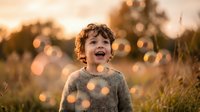 Young curly-haired boy laughing joyfully in golden sunset light with warm bokeh effects in natural outdoor setting for family lifestyle content.