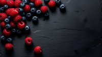 Fresh mixed berries strawberries and blueberries scattered on dark slate background with copy space for healthy eating and organic food concepts.