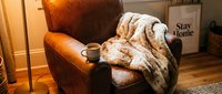 Cozy living room corner with a brown leather armchair, faux fur blanket, and steaming mug, creating a warm hygge atmosphere for relaxation at home.