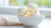Creamy vanilla ice cream scoops served in white ceramic bowl against bright window background, soft natural lighting highlights smooth texture and delicate swirls.