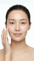 Young Asian woman applying white facial cream moisturizer on clean skin during daily skincare routine against white background for beauty and wellness.