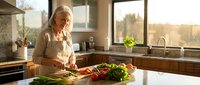 Senior Caucasian woman preparing fresh vegetables in modern kitchen during golden hour. Healthy cooking lifestyle for mature adults at home.