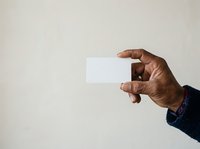 Man with dark skin tone holding blank white business card or paper against neutral background for branding and corporate mockup purposes.