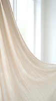 Sheer beige curtain fabric flowing gracefully with soft natural light streaming through window, creating elegant draping effect for interior design and home decor projects.