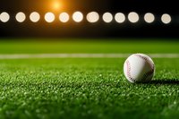 Baseball on green artificial turf field at night with stadium lights creating bokeh effect in background, dramatic sports atmosphere for game concepts.