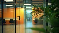 Modern office interior with glass doors and tropical plant in foreground, warm lighting creates welcoming atmosphere for business and corporate design concepts.