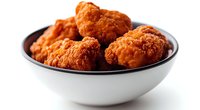 Crispy fried chicken pieces served in white ceramic bowl on dark background. Golden brown breaded chicken wings with crunchy coating for restaurant menu or food delivery.