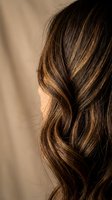 Close-up of woman's wavy brown hair with golden highlights showing natural texture and shine for beauty and haircare concepts.