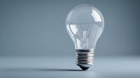 Clear glass light bulb with visible filament on minimalist gray background, symbolizing ideas, innovation, and creative thinking for business concepts.