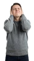 Young Caucasian man covering ears with hands wearing gray sweater expressing stress pain or loud noise on white background isolated for design use.