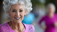 Cheerful senior woman with white curly hair and bright smile wearing purple sweater looking at camera. Active aging and wellness concept for elderly lifestyle.