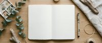 Open blank notebook with pen on wooden desk surrounded by eucalyptus branches, twine, and natural craft supplies for creative writing and planning.