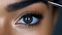 Close-up of woman's eye with professional makeup, long eyelashes, and defined eyebrow being shaped with cosmetic brush. Perfect for beauty tutorials.