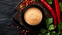 Spicy seasoning powder in black bowl on dark wooden board with fresh red chili peppers, crushed pepper flakes and parsley leaves on slate background.