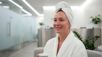 Young Caucasian woman in white bathrobe and towel headwrap smiling at modern spa wellness center with relaxation treatment skincare routine.