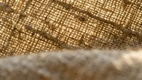 Natural burlap fabric texture with rustic weave pattern and wooden surface edge for organic design projects and craft backgrounds.
