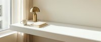 Minimalist workspace with golden mushroom lamp, coffee cup and notebook on white desk by window in warm natural light for modern home office design.