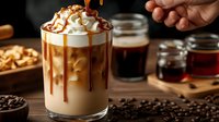 Layered iced coffee drink with whipped cream and caramel drizzle in glass, surrounded by coffee beans and honey jars on wooden surface, dark background.