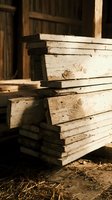 Stack of weathered wooden planks in rustic workshop setting with warm natural lighting for construction and carpentry projects.
