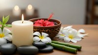 Spa wellness setup with burning candle, plumeria flowers, bamboo sticks, black stones and hibiscus tea bowl for relaxation and aromatherapy treatments.