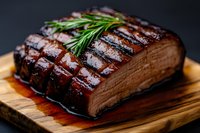 Grilled beef brisket with rosemary garnish on wooden cutting board, showing juicy meat texture and crosshatch grill marks in dark moody lighting.