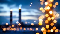 Dreamy defocused city lights create magical bokeh effect against blue twilight sky, industrial chimneys silhouettes visible in background. Atmospheric urban nightscape.