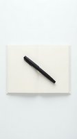 Black pen resting on open blank notebook with cream pages, isolated on white background, ready for writing, design, and educational use.